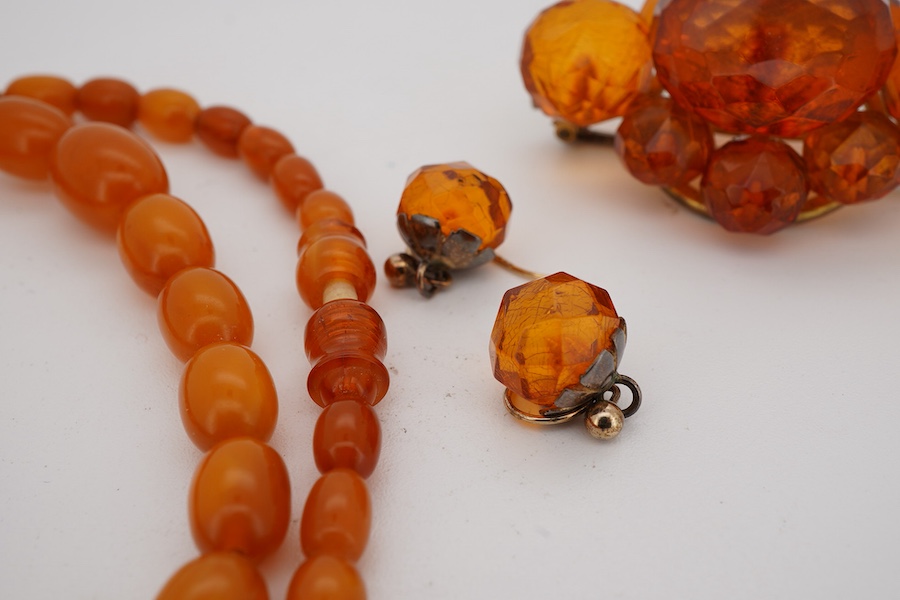 A single strand graduated oval amber bead necklace, 40cm, gross weight 9 grams, together with an amber cluster set brooch and pair of earrings.